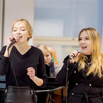 Kuvassa on kaksi opiskelijaa laulamassa mikrofoneihin.